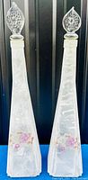 Front view of both frosted crystal decanter vases with floral decoration and stoppers visible on top.
