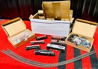 Wide shot showing multiple HO scale locomotives, freight cars, track sections laid out on a red surface with boxes in background