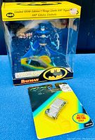Front view of the Batman 100th Edition figure sealed in display box and the Two-Face armored car sealed on card twin pack.