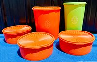 Set of 5 vintage Tupperware containers with lids, 4 orange and 1 light green, displayed on blue fabric.