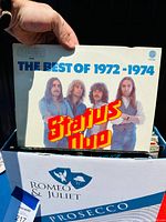Photo of a vinyl album cover 'The Best of 1972-1974' by Status Quo held above a box of records.