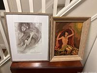 Two framed artworks on a wooden surface, showcasing both the mid-century modern painting and the framed Shape of Water poster.