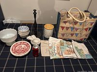 All items in the lot displayed on table, showing ceramics, measuring cups, towels, tote bag, and paper towel holder