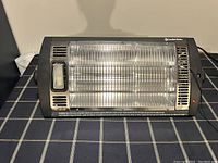 Front view of black ceiling mounted dual quartz heater with metal safety grill and pull string control on right side, integrated light on left side.