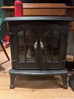 Closed electric fireplace with glass double doors and metal handles, showing overall stove design and size compared to soda can on top.