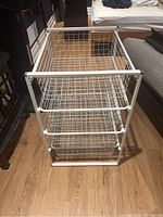 Front view of white IKEA Antonius storage unit with four wire baskets, showing basket spacing and metal frame structure