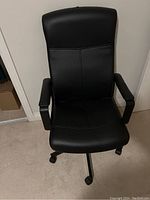 Front view of black IKEA swivel office chair showing cushioned seat, backrest, and armrests on caster wheels.