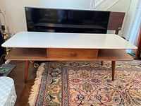 Front view of coffee table showing white laminate top, teak frame, open shelf and drawer