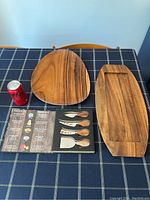 Top view of both teak trays and cheese spreader set on checkered tablecloth with soda can for scale