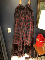 Photo of two deep red and black tartan fleece dressing robes hanging on hooks, showing the full length and pattern.