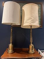 Pair of vintage brass table lamps seen from the front with different lampshades on wooden surface.