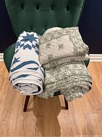 Two quilts folded and placed on a green chair showing green floral quilt with matching pillowcases and a white and blue star patterned quilt.