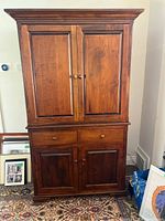 Front view of the solid wood media armoire with closed upper and lower doors and two drawers in between.