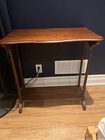 Front view of the side table showing spindle legs and lower shelf against a dark wall with wooden floor.