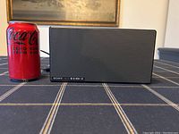 Front view of Sony SRS-X55 speaker next to Coca Cola can for scale, showing metal mesh grille and branding.