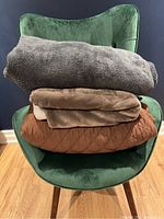 Stack of three large throw blankets on a green chair: brown quilted, soft plush brown, and beige fleece throw