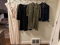 Four hanging garments side by side on hangers: a light beige sleeveless long dress, a black dress, an olive-green dress with rolled sleeves, and a denim jean jacket.