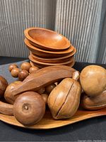 Photo showing five wooden bowls stacked and eleven wooden fruit pieces on a wooden tray.