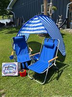 Photo showing the full beach setup with shelter, two blue folding loungers, boxed inflatable boat, and colorful pails on grass.