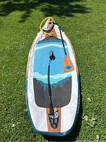 Full view of inflated paddle board on grass with paddle, pump and leash.