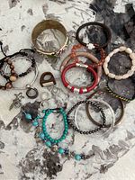 Top view of assorted bracelets, rings, and bangles arranged on a patterned surface showing variety of materials including wood, leather, beads, and metal.
