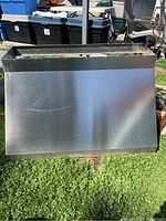 Front view of stainless steel kitchen hood fan cover showing overall size and condition outdoors on grass.