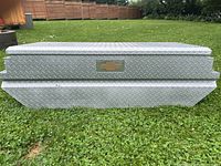 Front-facing photo of the aluminum under rail truck box showing diamond plate texture and Chevrolet emblem.