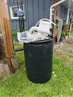 Full view of the dark green 50 gallon rain barrel outdoors with assorted hoses and white diverter on top.