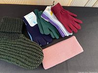 Photo showing dark green chunky knit slippers alongside six pairs of knit gloves in various colors including green, red, purple, white, navy blue.