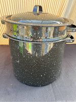 Full view of graniteware pot with steamer insert and lid on top, black with white speckles.