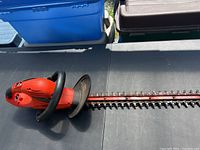 Full view of the orange hedge trimmer showing the cutting blade and handle with hand guard.