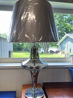 Full view of the large accent lamp showing silver base, smoked glass body, and wrapped conical lampshade in a window setting.
