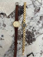 Both watches side by side on a marble surface showing their straps and dials clearly.