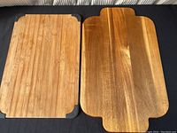 Two wooden cutting boards laid flat on black cloth, showing bamboo Sabatier cutting board with black corner grips on left, and natural wood cutting board on right