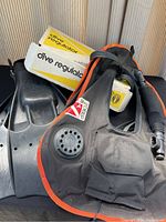 Photo showing Black White Stag Deep BCD with orange trim, Aqualung regulator, and black Scubapro Jetfin fins piled together, showing BCD front valve and fins.