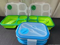 Two green collapsible lunch kits with sections and utensils, stacked blue double-decker lunch kit in front