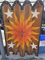 Full view of four-panel wooden room divider showing large sun face in middle with white stars on each side, scalloped edges and dark painted trim.