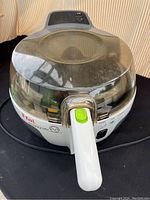 Front view of a white and grey T-fal Actifry air fryer with a transparent lid and a green button on the handle.
