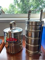Two stainless steel tiffin tins placed side by side showing their height and structure on a wooden surface.