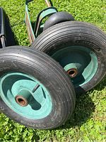 Two new black rubber wheelbarrow tires with green metal rims placed on grass.