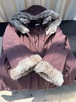 Front view of burgundy winter coat showing arms and faux fur lined sleeves and hood.