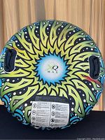 Top view of the round XQ Max floatie showing colorful sunburst design and black handles.