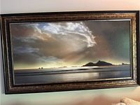 Framed oil painting showing water, island, and clouds with dramatic lighting and a reflective water surface.