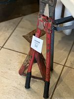 Medium bolt cutter standing upright, showing red handles and black grips, placed on a tiled floor.