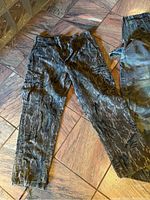 Dark grey camouflage cargo pants with multiple pockets lying flat on wood floor.