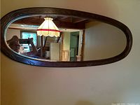 Front view of the full oval mirror mounted on a wall reflecting a ceiling lamp and room interior