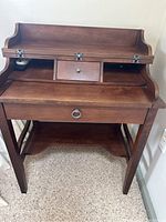Front view of solid wood secretary style desk with fold-down writing surface and small central drawer open.