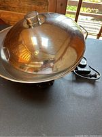 Faberware electric wok with lid showing dome shape and knob handle, rests on black surface.
