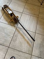 Metal 3 ton floor jack with long handle, viewed from an angle on tile flooring.