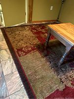 View of the multi-colored Karastan rug under a wooden table showing red, brown, and green patchwork with floral and vine designs.